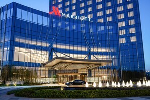 A Marriott hotel with a modern glass facade, a covered entrance, and a fountain display.