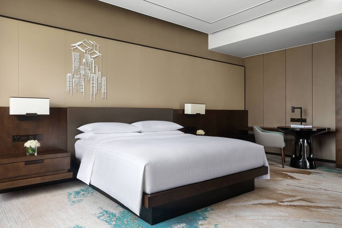 A modern hotel room with a large bed, bedside tables, a desk, and a chair.