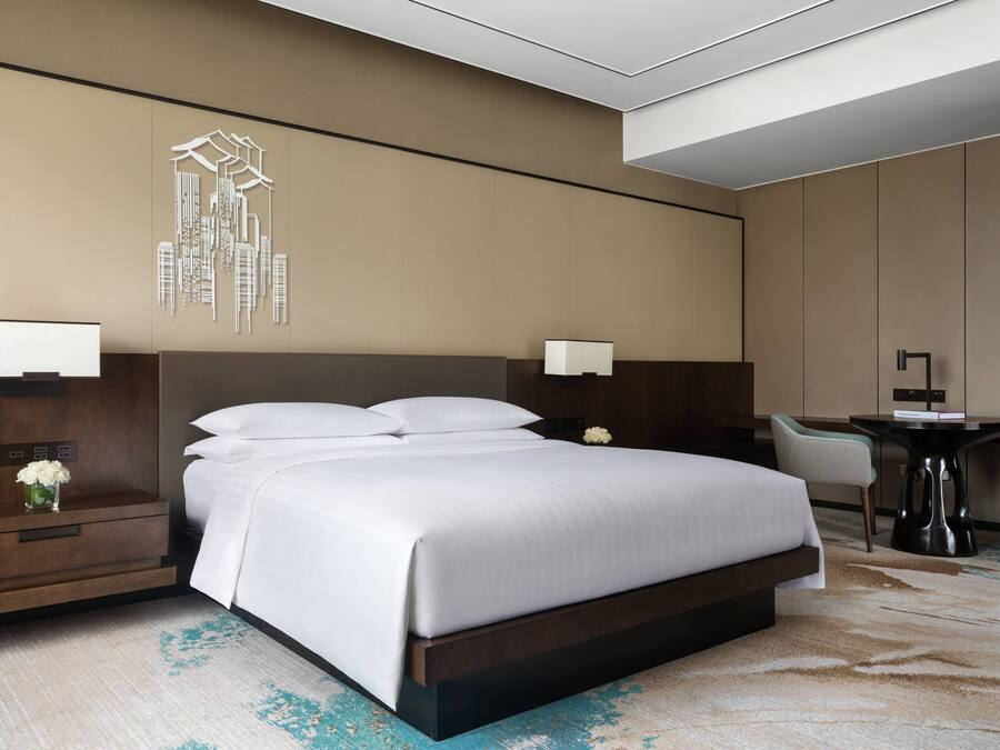 A modern hotel room with a large bed, bedside tables, a desk, and a chair.