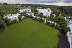 Um edifício grande e branco, com vários andares, e um pátio central rodeado por vegetação exuberante e palmeiras.