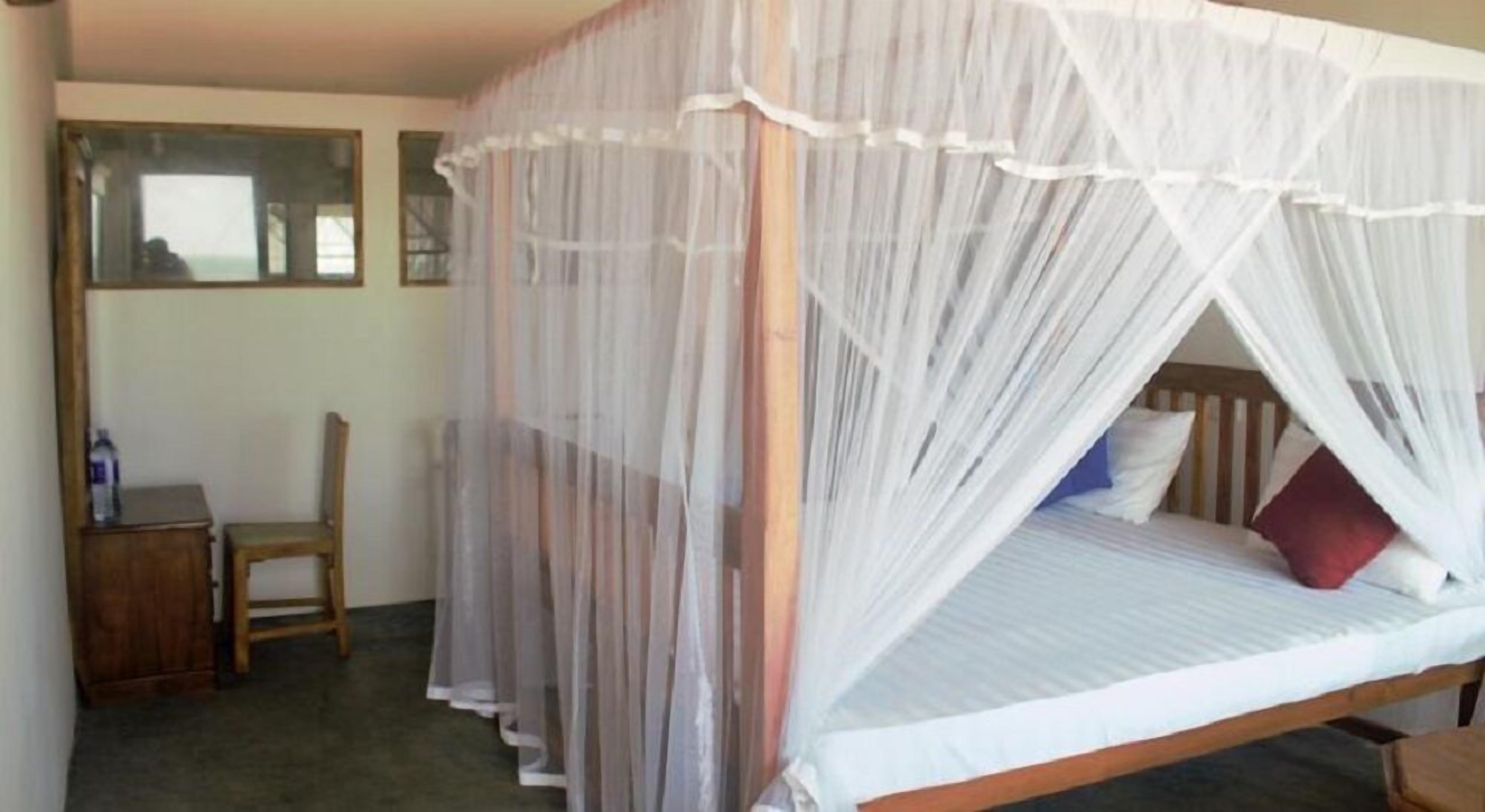 A single bed with a canopy, a wooden chair, and a small table with a bottle on it.