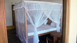 A single bed with a white canopy in a room with a wooden floor and a chair. - Asiri Yoga Retreat (Boossa)