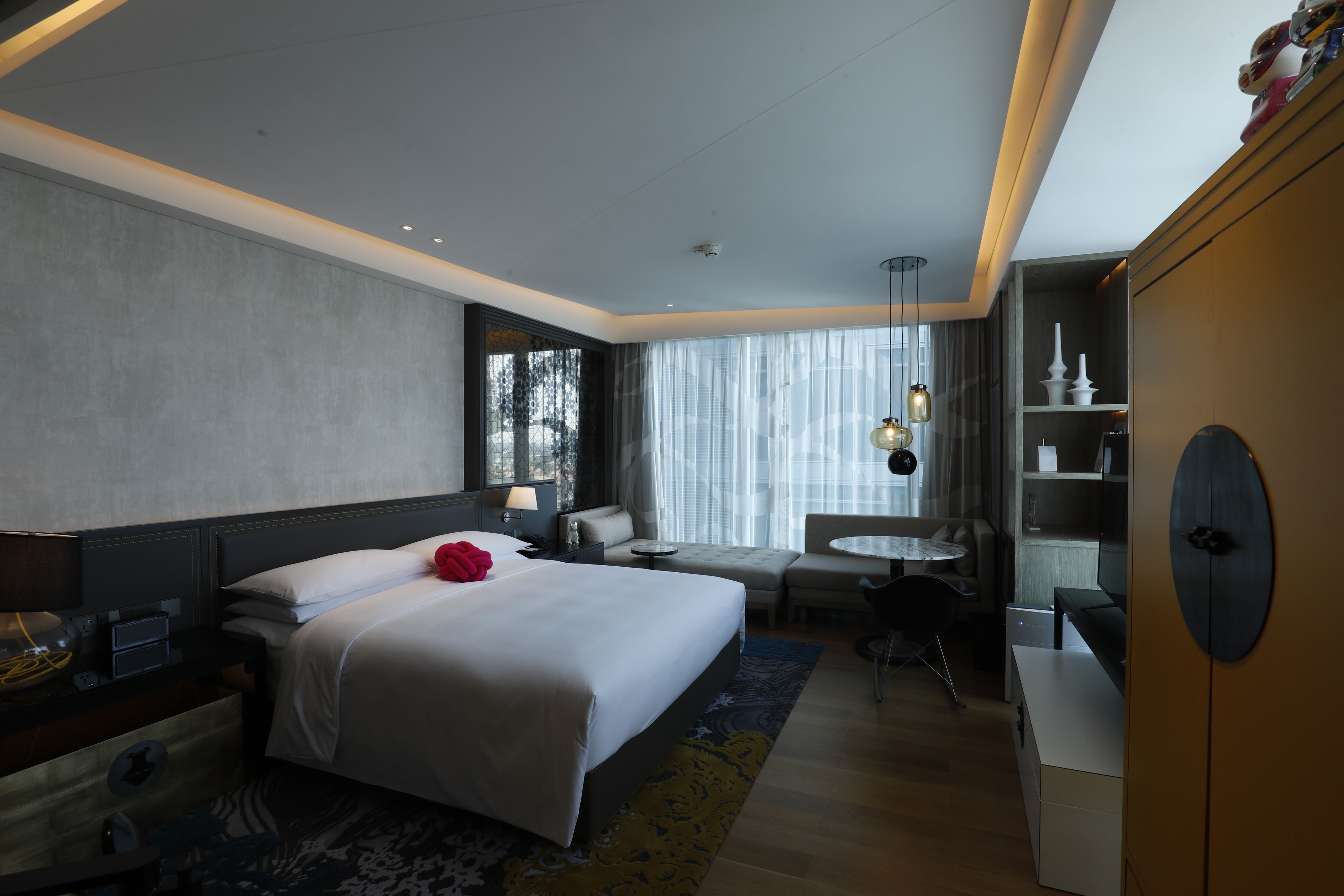 A modern hotel room with a large bed, bedside tables, a desk, a chair, and a small round table.