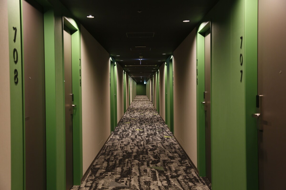 A hotel hallway with green doors numbered 708 and 707, carpeted floor, and a ceiling with recessed lighting.