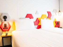 A hotel room with a bed, a nightstand with a lamp, and a wall with geometric patterns.