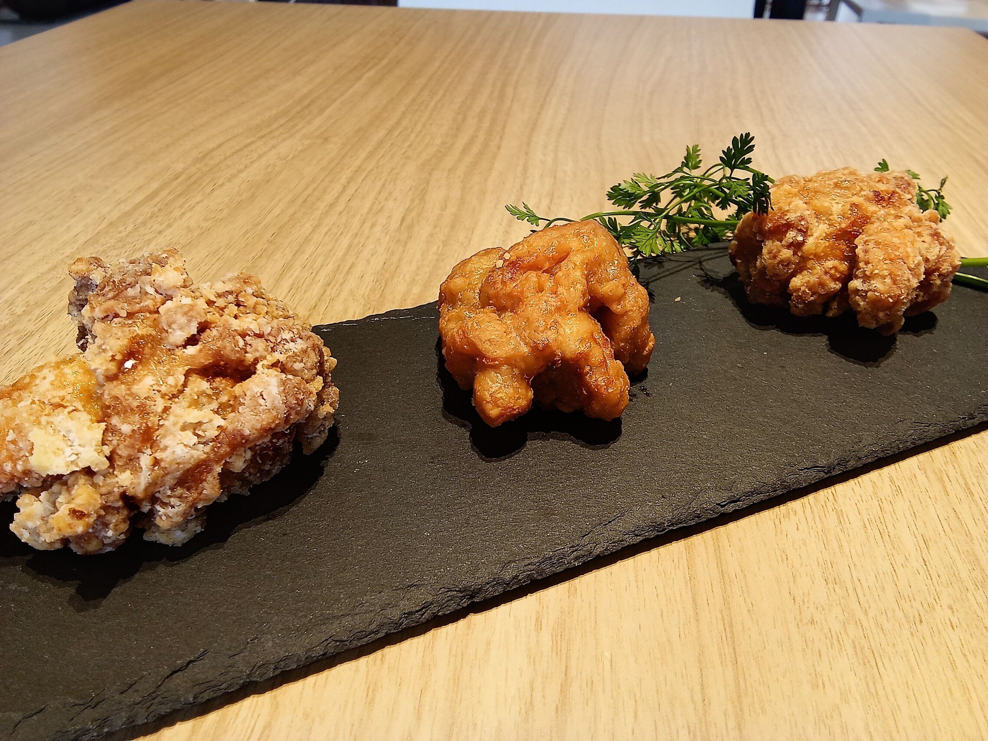 A black slate serving board with three pieces of fried chicken on a wooden table.