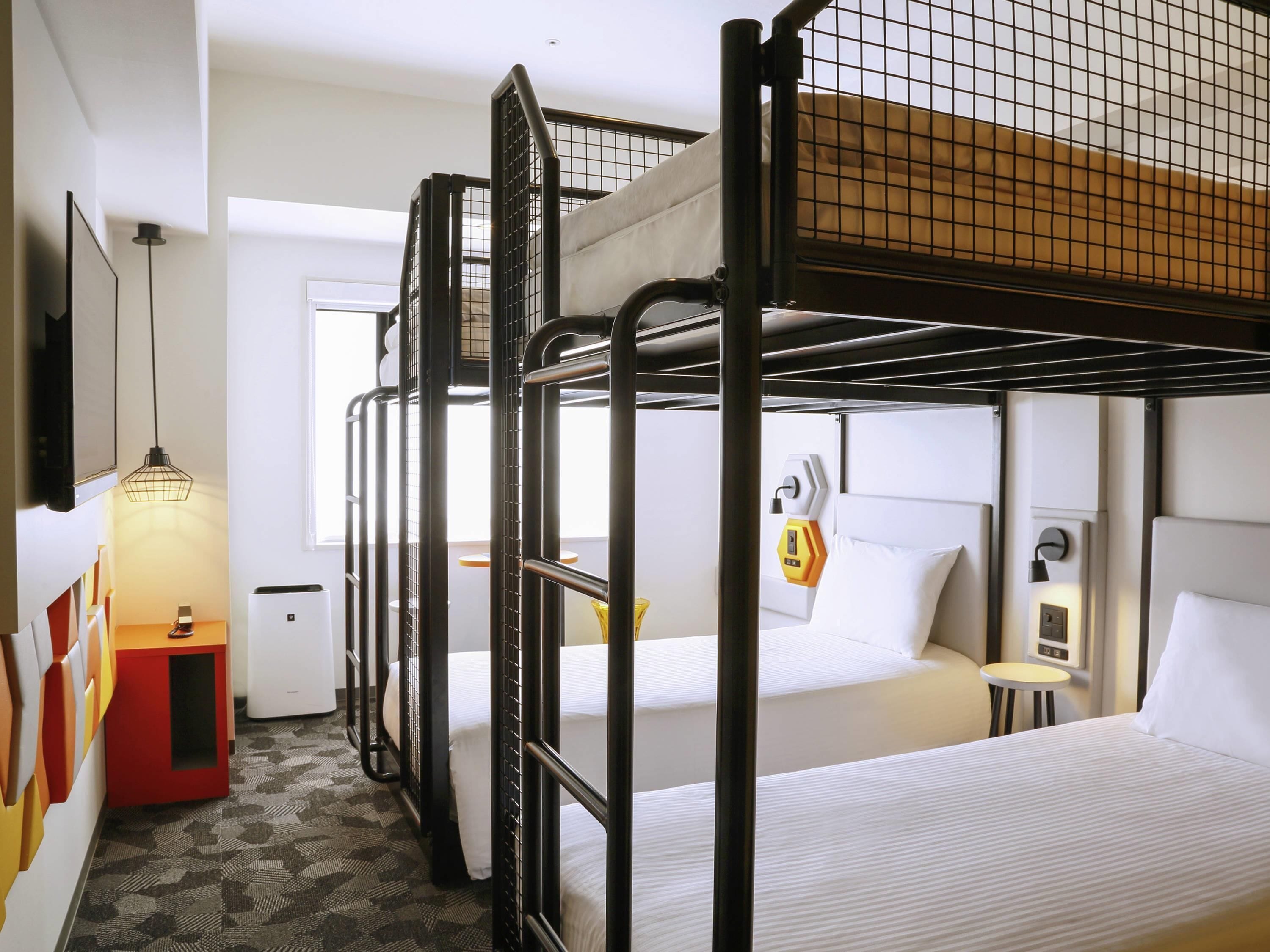 A bunk bed room with a desk, a small table, and a wall-mounted heater.