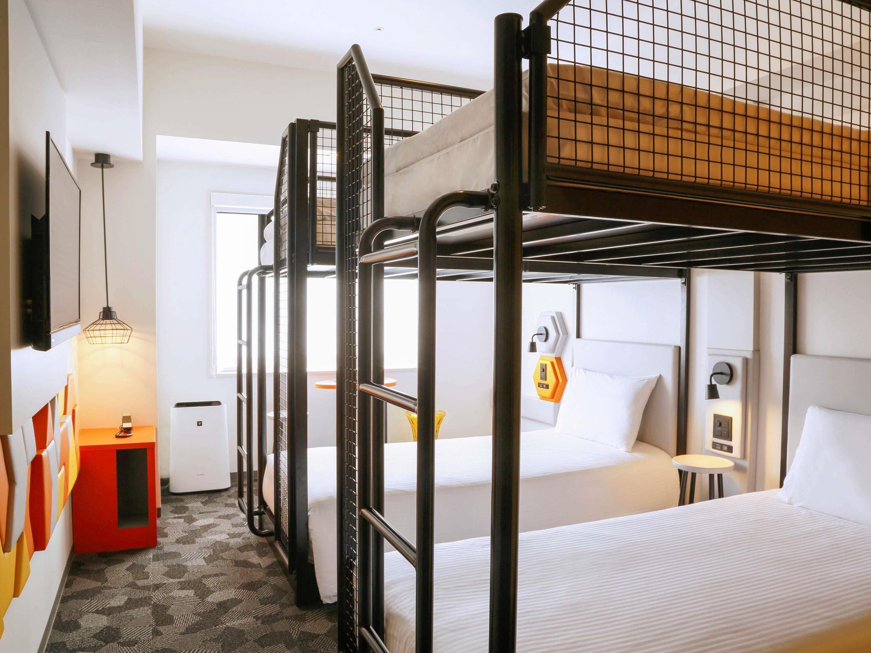 A bunk bed room with a desk, a small table, and a wall-mounted heater.
