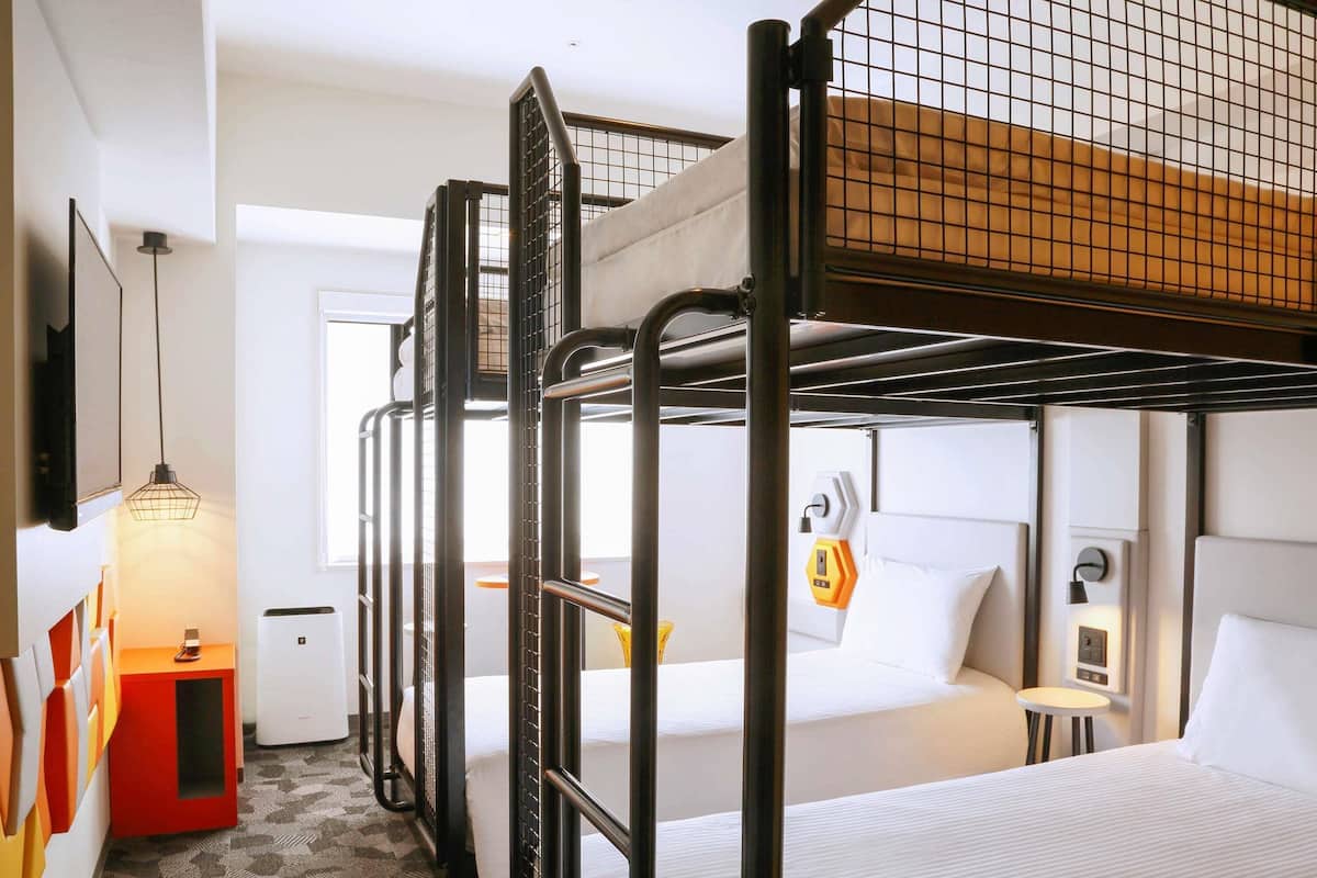 A bunk bed room with a desk, a small table, and a wall-mounted heater.