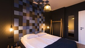 Um quarto moderno com padrão de parede quadriculado, cama com roupa de cama branca, luminária pendente e uma escada de madeira encostada na parede.