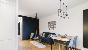 Um espaço de estar moderno com uma parede de destaque azul escuro, uma mesa de jantar de madeira e um sofá com almofadas.
