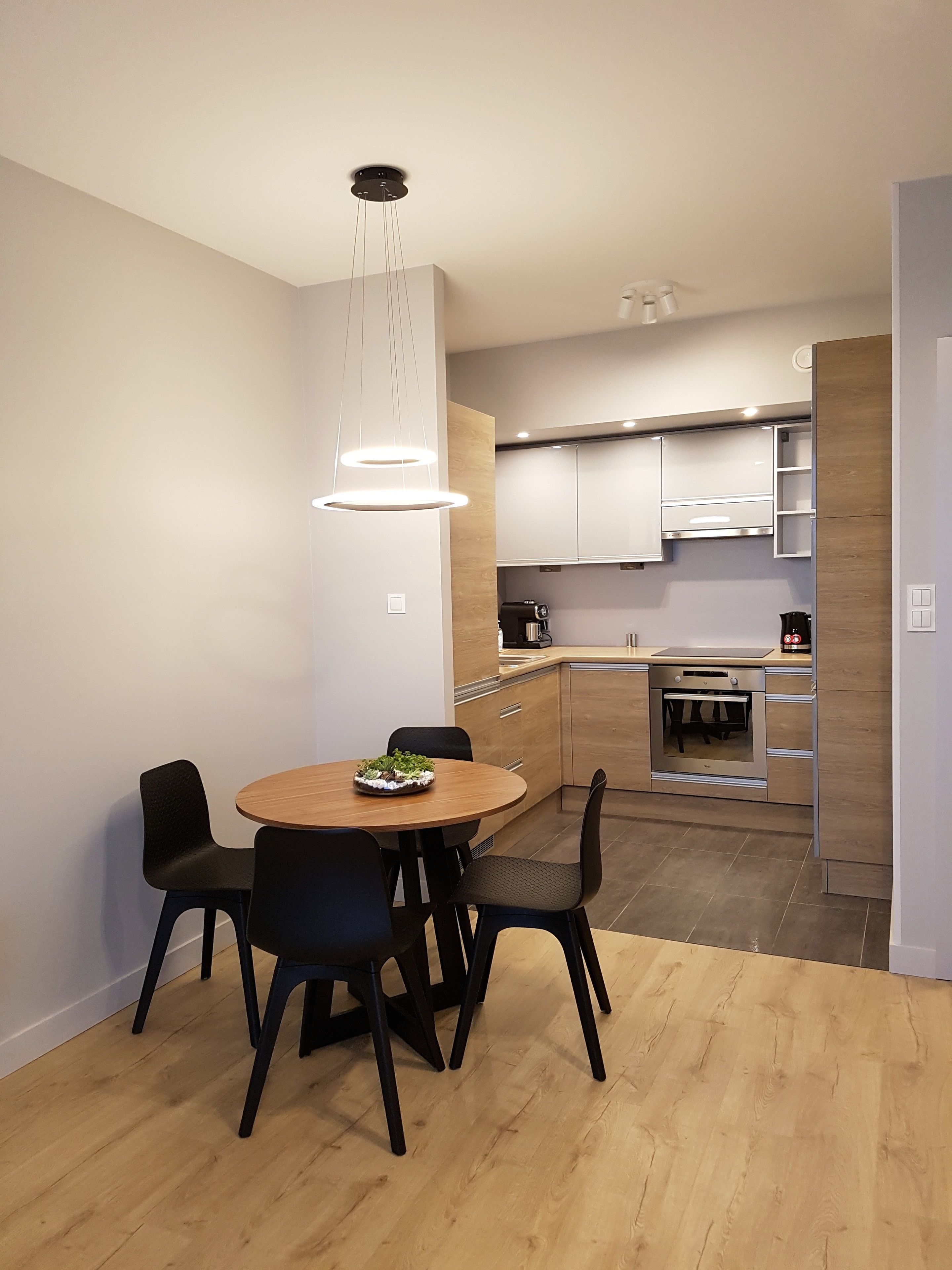 Cocina moderna con armarios de madera, horno empotrado y comedor con mesa y sillas redondas.
