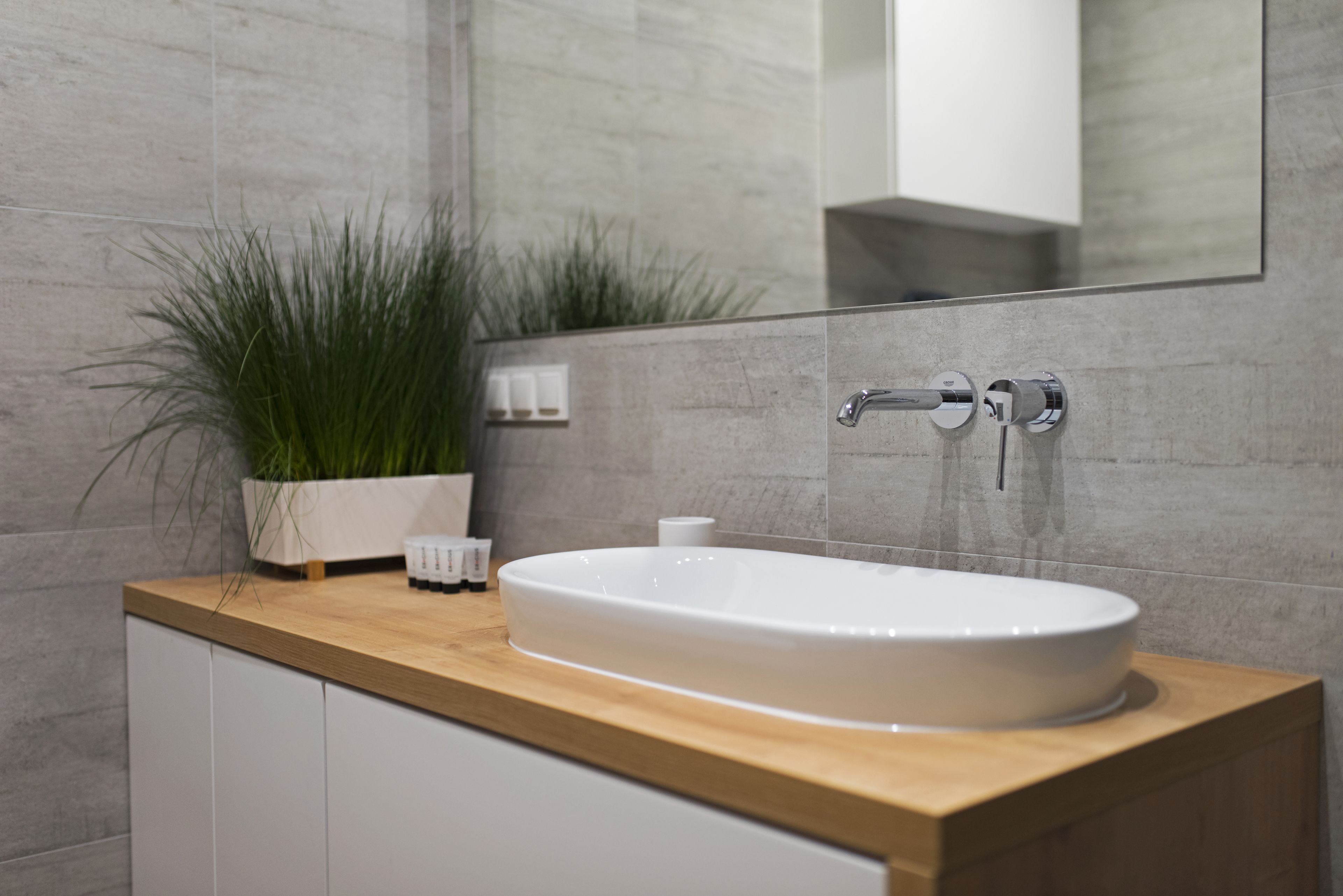 Ein modernes Badezimmer mit einem weißen Waschbecken, einer Holzablage und einem großen Spiegel.