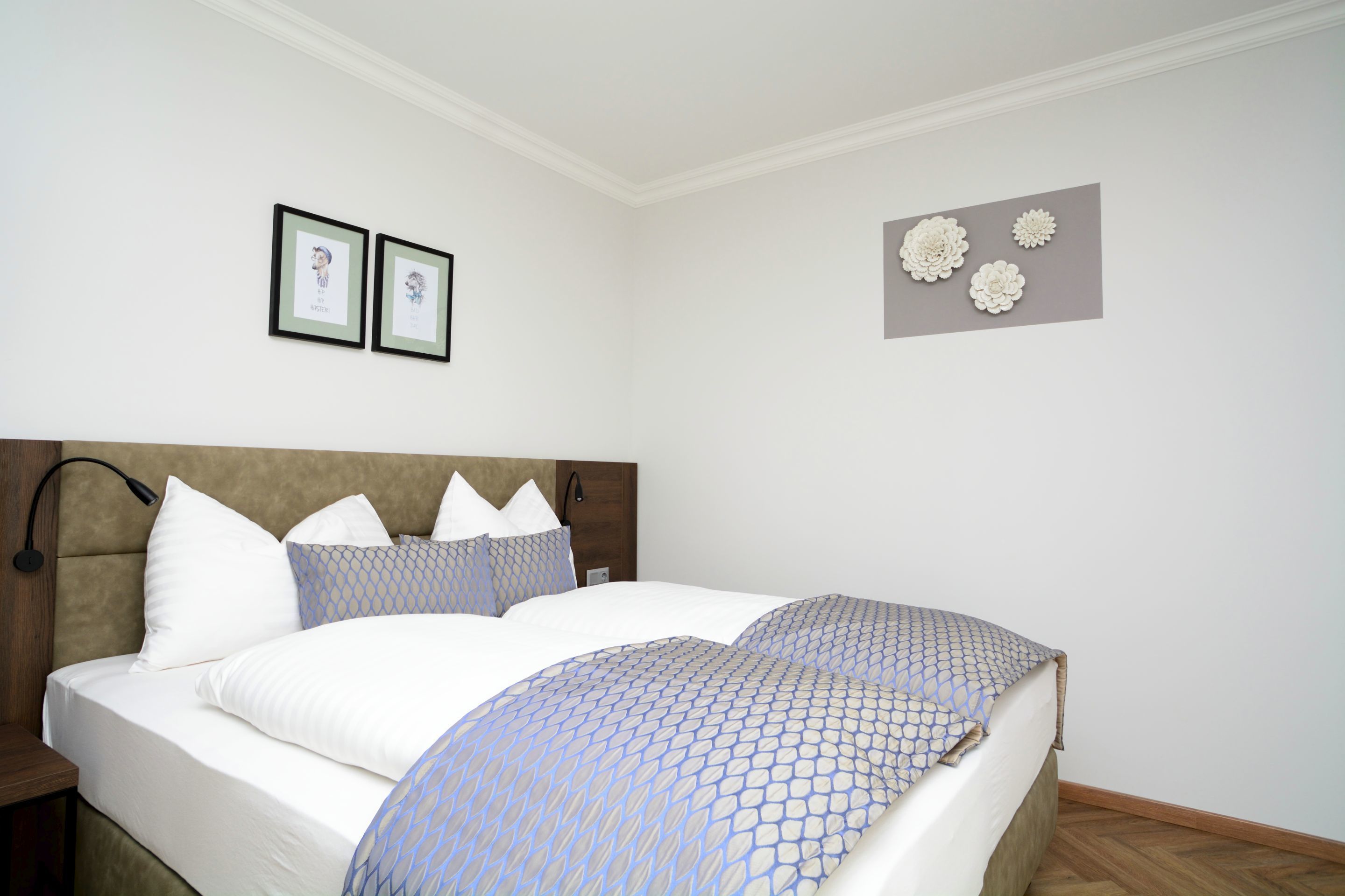A neatly made bed with a patterned bedspread, a wooden headboard, and two framed pictures on the wall.