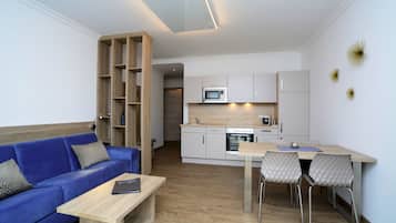 Apartamento moderno com sofá azul, mesa de centro de madeira e cozinha com armários brancos e micro-ondas.