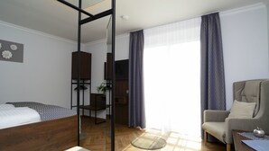 A modern hotel room with a wooden bed, a seating area with a chair and table, a desk with a computer, and a large window with curtains. - Apart of me Villach (Villach)