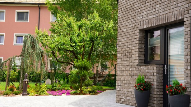 A modern building with a brick facade, large windows, and a well-maintained garden with various plants and flowers. - Apart of me Villach (Villach)