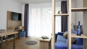 A modern living room with a wooden floor, a blue sofa, a coffee table, a TV mounted on a wooden panel, and a bookshelf with a bottle. - Apart of me Villach (Villach)