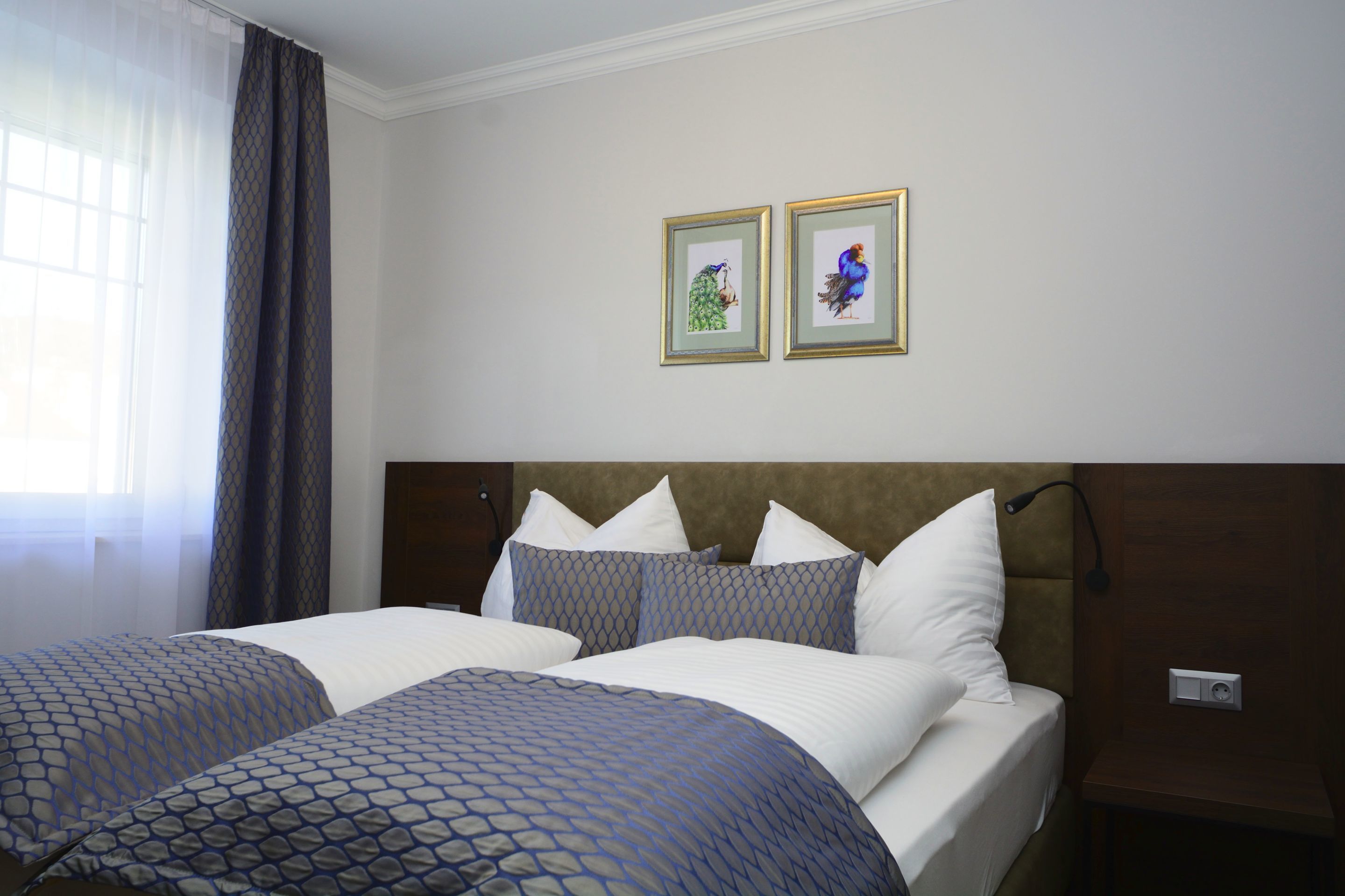 A hotel room with two beds, a headboard, a nightstand, and two framed pictures on the wall.