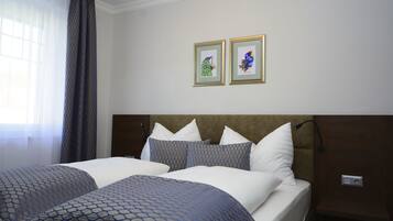 A hotel room with two beds, a headboard, a nightstand, and two framed pictures on the wall.