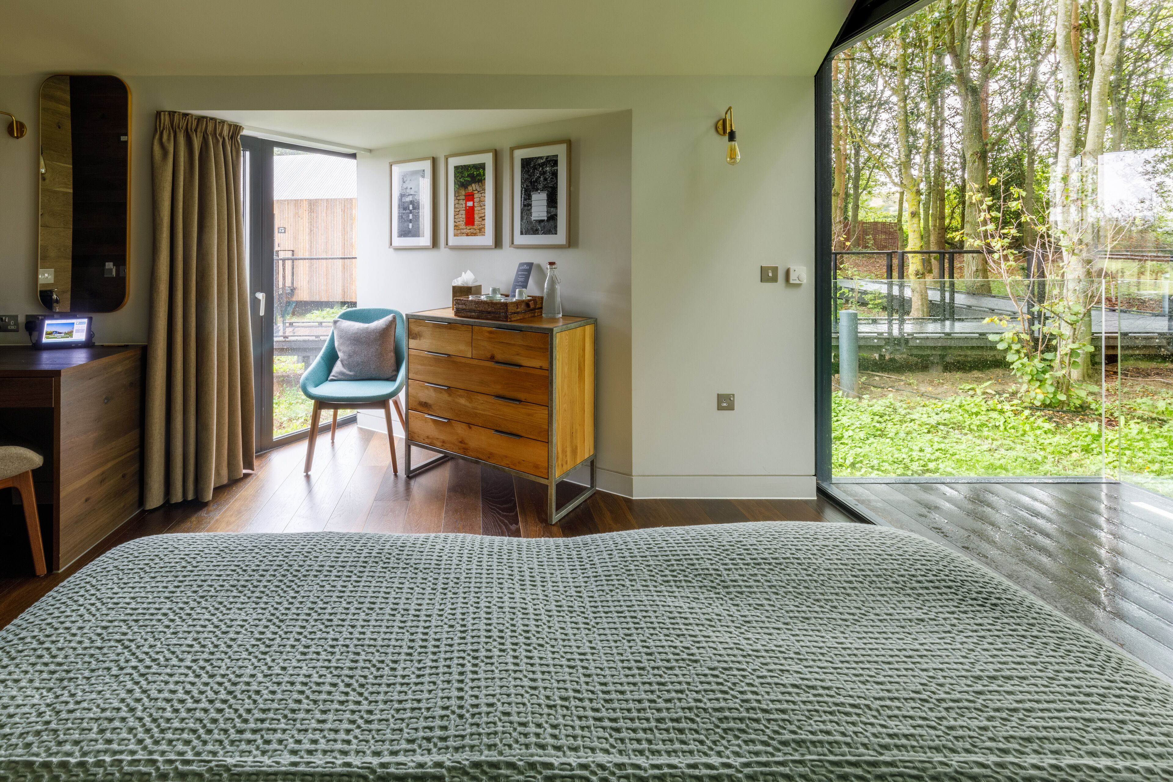 A bedroom with a large bed, a wooden dresser, a chair, and a desk. There is a window with a view of trees and a fence.