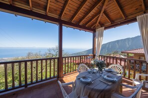 A covered outdoor dining area with a table set for two, overlooking a scenic view of the sea and mountains. - Villa de Montaña Ilusión (La Orotava)