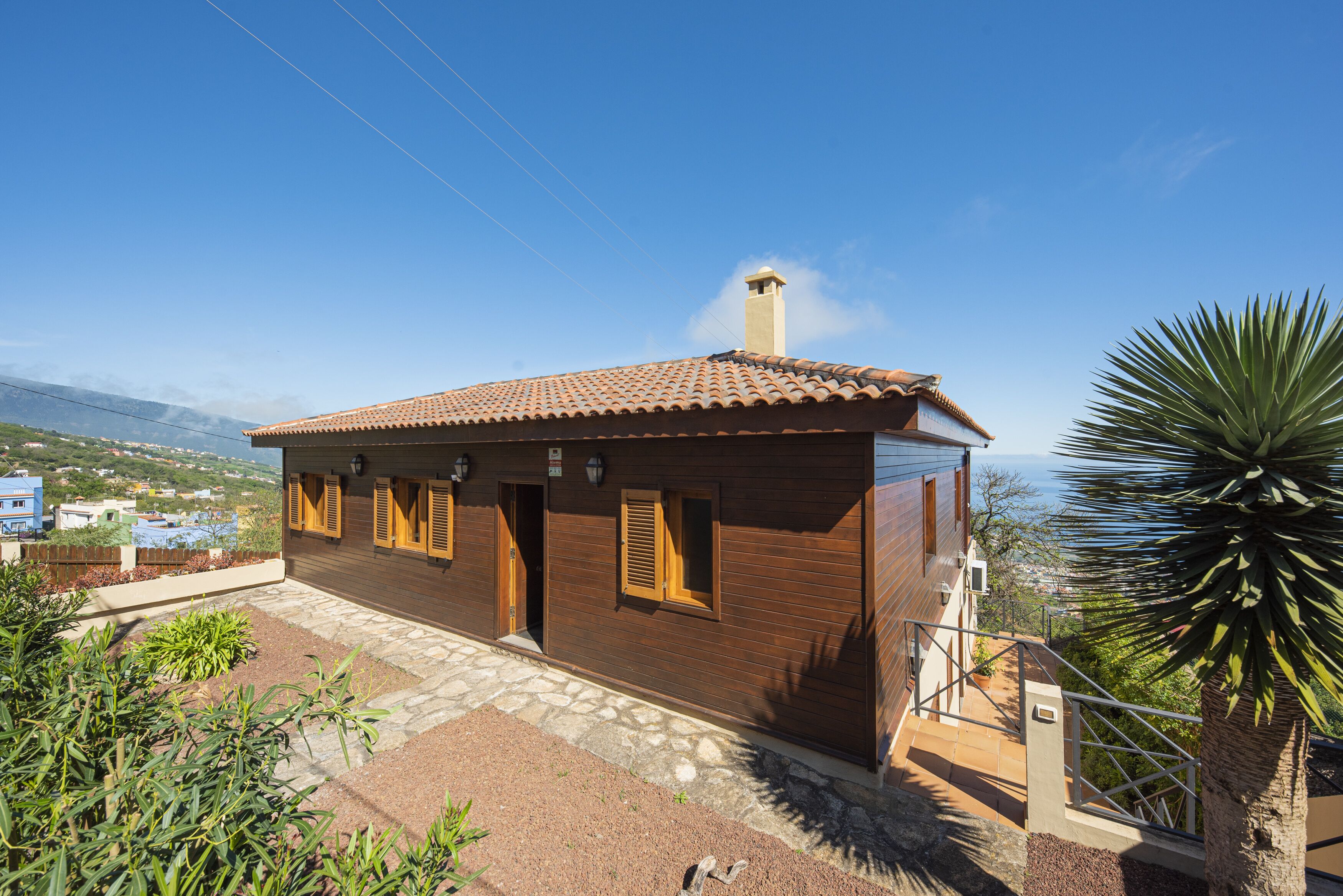 A wooden house with a tiled roof, a chimney, and a stone pathway leading to the entrance.