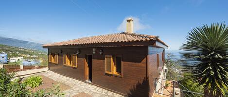 A wooden house with a tiled roof, a chimney, and a stone pathway leading to the entrance.