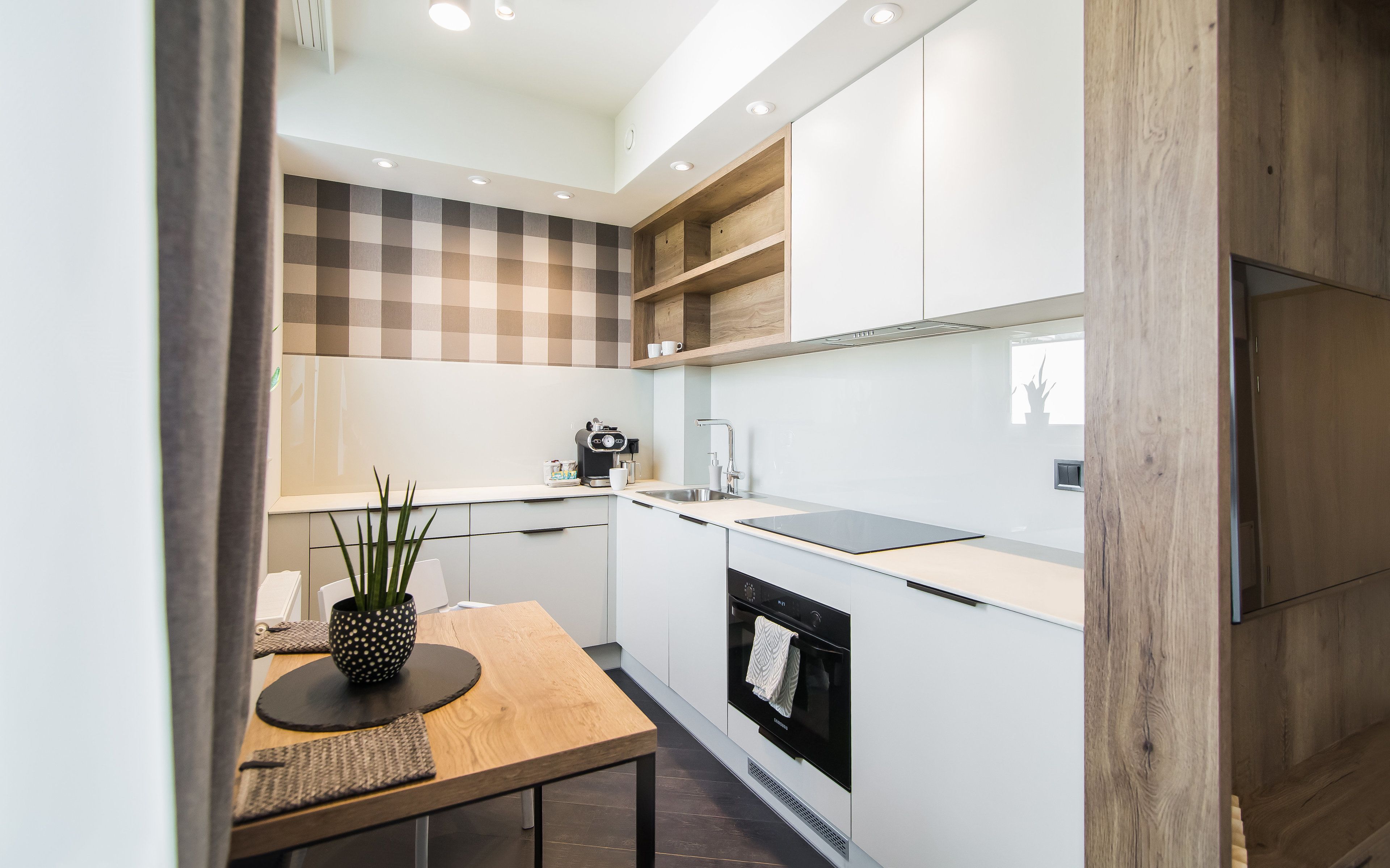 A modern kitchen with white cabinets, a wooden table, and a built-in oven.