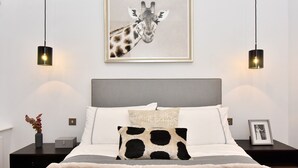 A bedroom with a bed, a framed giraffe picture, two bedside lamps, a nightstand, and a framed photo. - Light-Filled, Contemporary Retreat near The Ritz (London)
