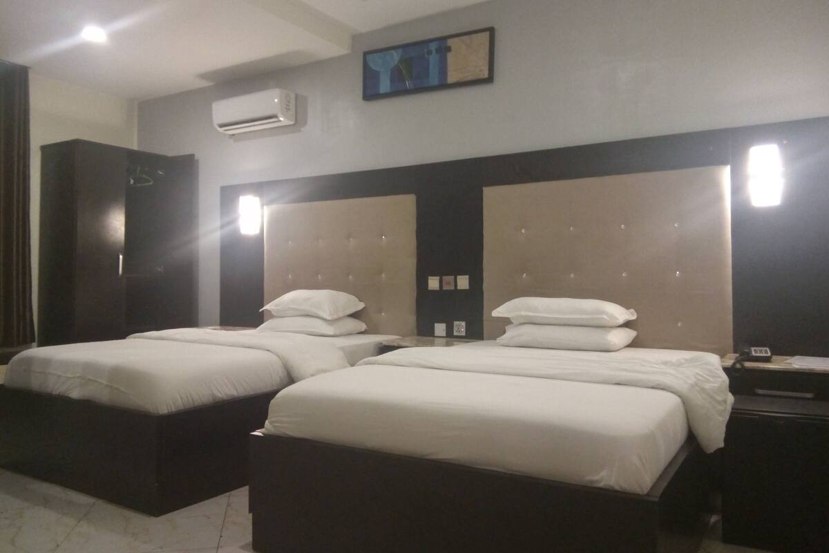 Habitación de hotel con dos camas, un armario, aire acondicionado y un cuadro en la pared.