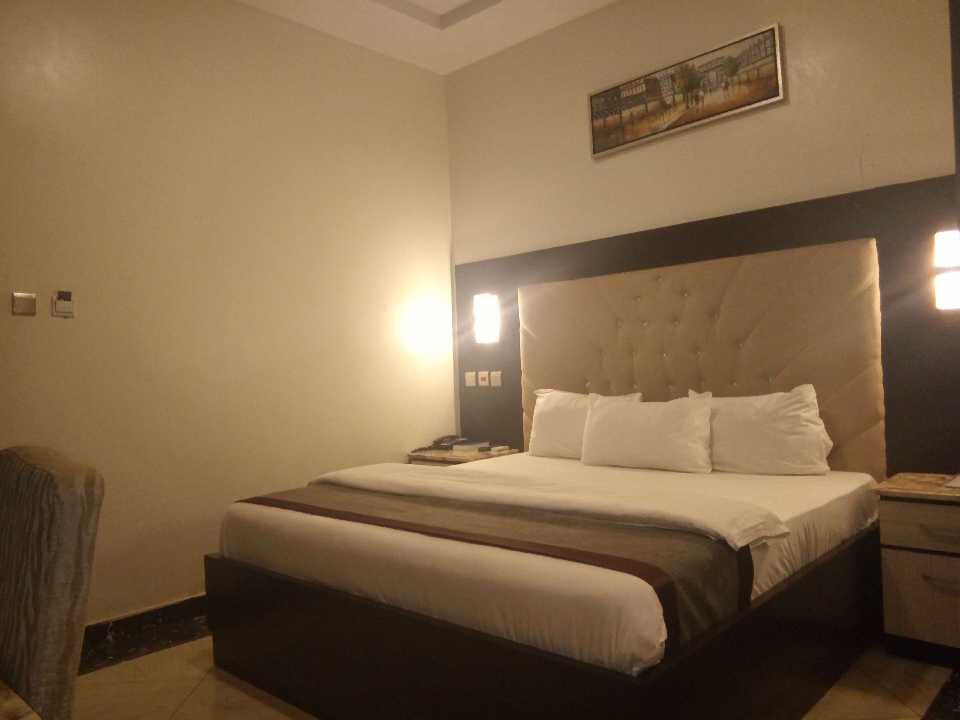 Une chambre d’hôtel avec un grand lit, une table de chevet, une chaise et un tableau au mur.