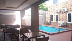 An outdoor pool area with a brick wall, air conditioning units, and outdoor seating. - De Gladys Hotel (Enugu)