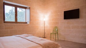 Un dormitorio con una cama, una ventana, una lámpara de pie, una silla y un televisor montado en la pared.