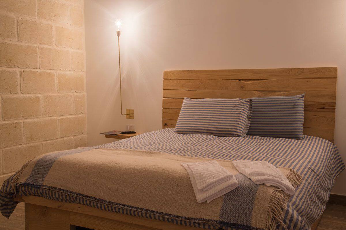 Un lit avec une tête de lit en bois, une literie à rayures et une table de chevet avec une lampe.