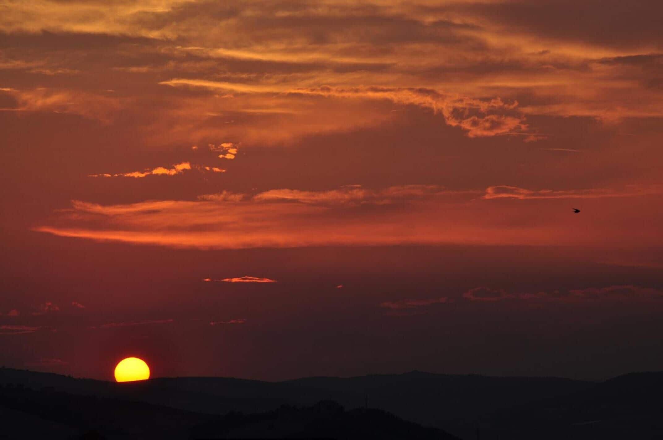 Un atardecer sobre un paisaje montañoso con un avión visible en el cielo.