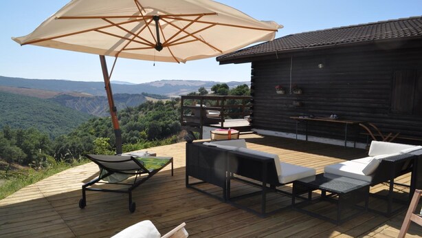 Una terraza de madera con mobiliario exterior, un paraguas grande y vistas al campo.