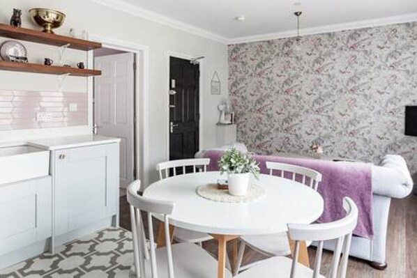 Uma cozinha moderna com armários brancos, uma mesa de jantar redonda e um cobertor roxo sobre um sofá branco.