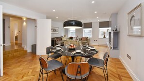 Un'area pranzo con un tavolo rotondo apparecchiato per sei persone, circondato da sei sedie. La stanza ha un pavimento in legno, pareti bianche e un soffitto con illuminazione a incasso.