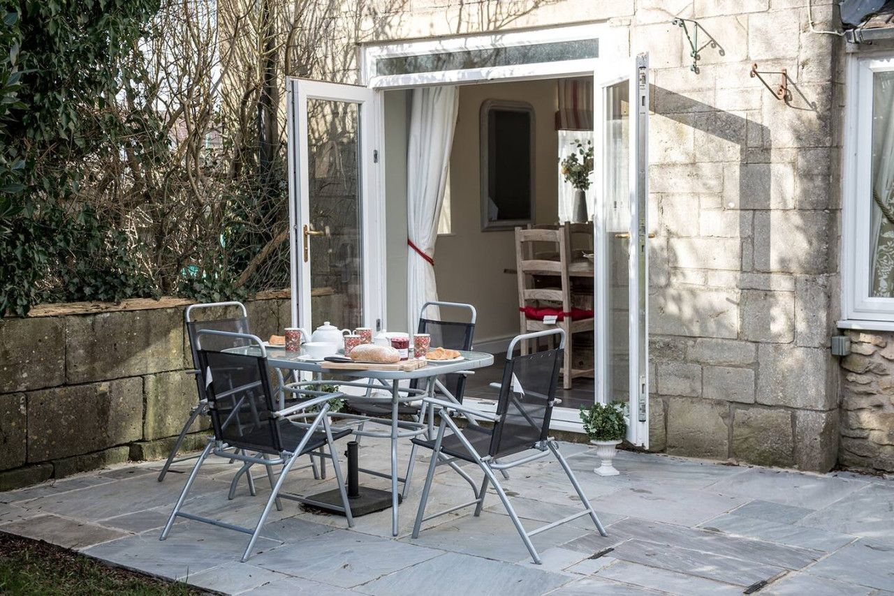 An outdoor patio with a table set for two, surrounded by chairs, and a door leading to an interior space.