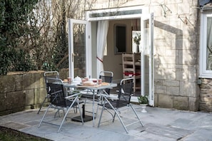 An outdoor patio with a table set for two, surrounded by chairs, and a door leading to an interior space. - Old Bakery Cosy Cottage in Bath - 3 Bedroom, Free (Bath)
