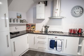 A modern kitchen with white cabinets, a black countertop, a gas stove, and a clock on the wall. - Old Bakery Cosy Cottage in Bath - 3 Bedroom, Free (Bath)