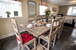 A dining area with a wooden table set for four, surrounded by wooden chairs with red cushions. - Old Bakery Cosy Cottage in Bath - 3 Bedroom, Free (Bath)