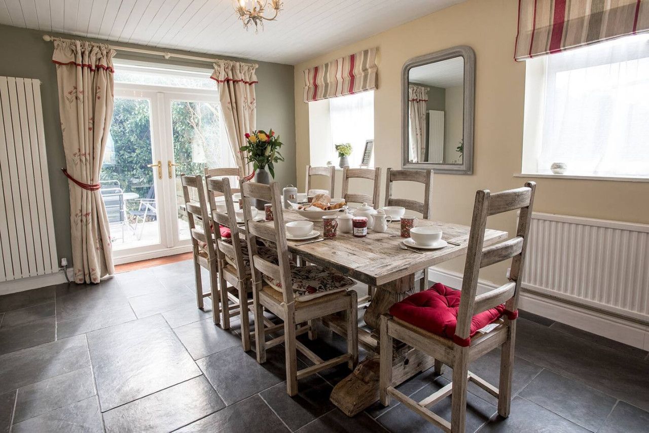 A dining area with a wooden table and chairs, a vase with flowers, and a window with curtains.