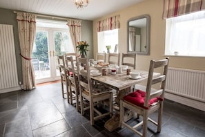 A dining area with a wooden table and chairs, a vase with flowers, and a window with curtains. - Old Bakery Cosy Cottage in Bath - 3 Bedroom, Free (Bath)