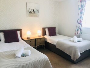 A hotel room with two beds, each with a pillow and a rolled towel. There is a nightstand with a lamp between the beds. - Old Bakery Cosy Cottage in Bath - 3 Bedroom, Free (Bath)