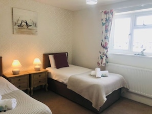 A bedroom with a single bed, a nightstand with lamps, a window with floral curtains, and a painting on the wall. - Old Bakery Cosy Cottage in Bath - 3 Bedroom, Free (Bath)