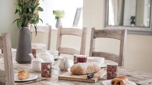 A rustic wooden table set with a loaf of bread, pastries, teacups, and a vase of flowers. - Old Bakery Cottage in Bath - 3 Bedroom, Free (Bath)