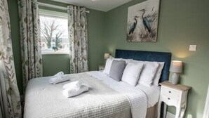 A neatly made bed with white linens and towels, a headboard, a bedside table with a lamp, and a painting of birds on the wall. - Old Bakery Cottage in Bath - 3 Bedroom, Free (Bath)