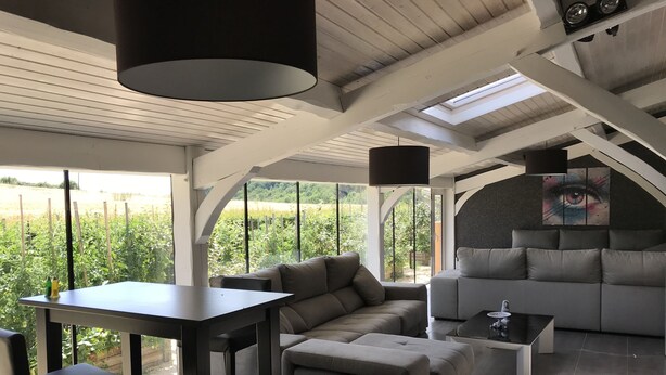 A modern interior with a sofa, a table, and a chair. There is a large window providing a view of greenery outside. - Les Chambres d'Hôtes du Mont Monnet (Longes)